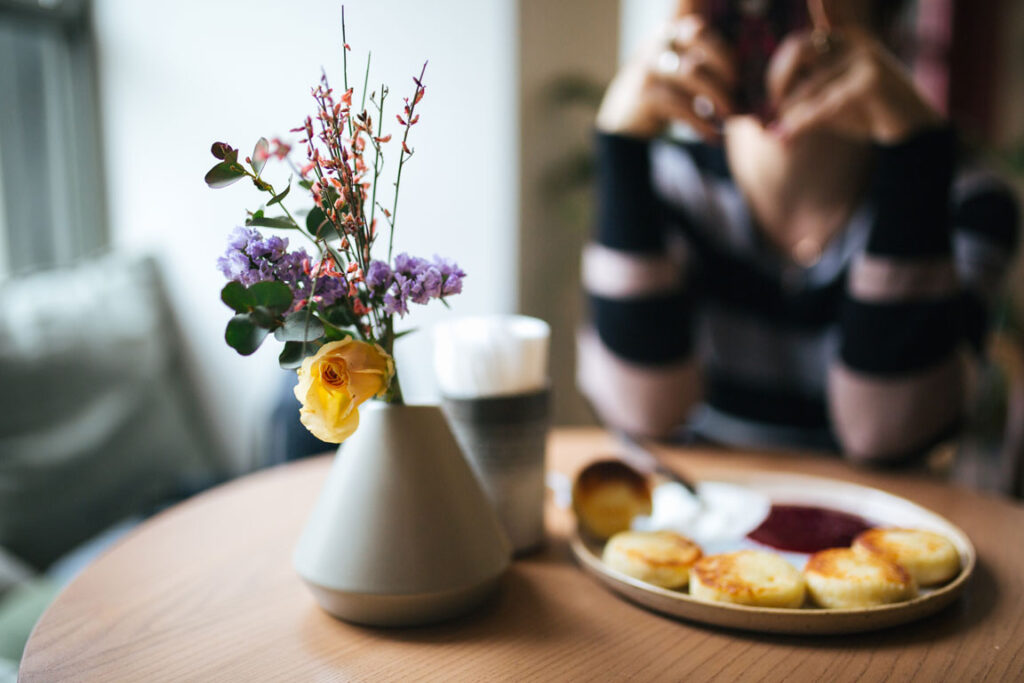 Breakfast and tea next to flowers on top of a table with framed pictures in the background.