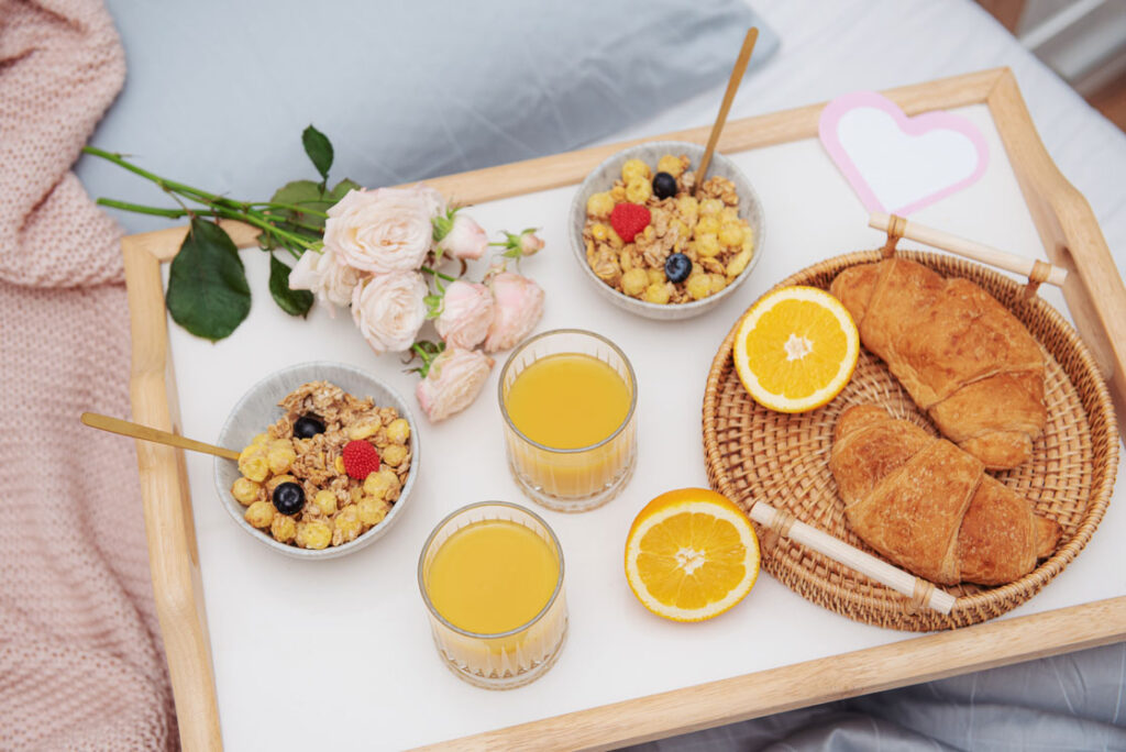 Breakfast of fruit, flowers and scones on a wooden tray served on top of a bed.