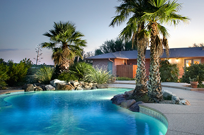 A serene pool surrounded by palm trees and a house, illuminated by the soft glow of dusk.